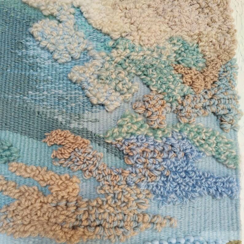 K&ouml;nnte beinhalten: Nahaufnahme einer gewebten Wandbeh&auml;nge mit einem strukturierten, abstrakten Design. Die Beh&auml;nge zeigt eine Vielzahl von Farben, darunter Blau, Gr&uuml;n und Beige.