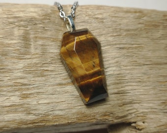May include: A gold and brown tiger's eye gemstone pendant in a coffin shape hangs from a silver chain.