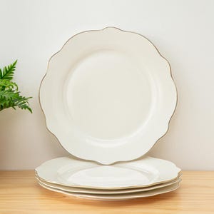 May include: Set of four white ceramic dinner plates with a scalloped edge and a thin gold rim.