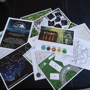 May include: A collection of printed game cards and instructions for a scavenger hunt themed around a camp called "Camp Nowhere". The cards feature images of constellations, a treasure chest, and a map with a compass.