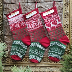 Könnte beinhalten: Drei rote und grüne Weihnachtsstrümpfe mit weißen Strickmustern. Die Strümpfe haben Holzetiketten mit den Worten "Papa", "Kinder" und "Mama" darauf.