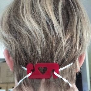 May include: Red plastic mask extender with a heart cutout. The extender is attached to a white elastic band.