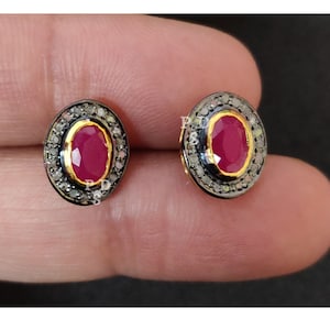 May include: A pair of oval-shaped ruby earrings with a halo of small diamonds set in silver and gold. The earrings are a classic and elegant design.