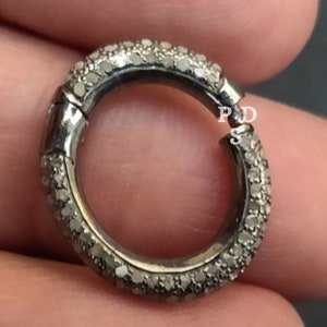 May include: A silver ring with a row of small diamonds around the band. The ring is open and has a clasp.