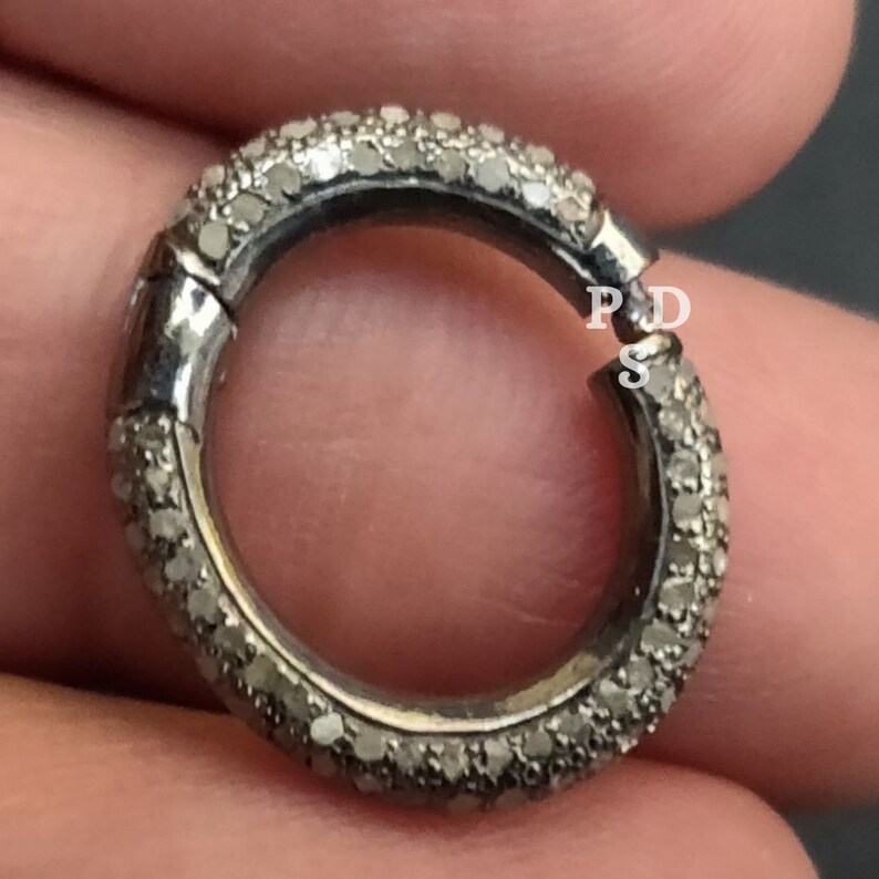 May include: A silver ring with a row of small diamonds around the band. The ring is open and has a clasp.