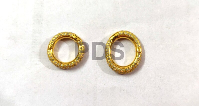 May include: Two gold-toned rings with a circular design. Each ring is adorned with small, white stones that create a sparkling effect.