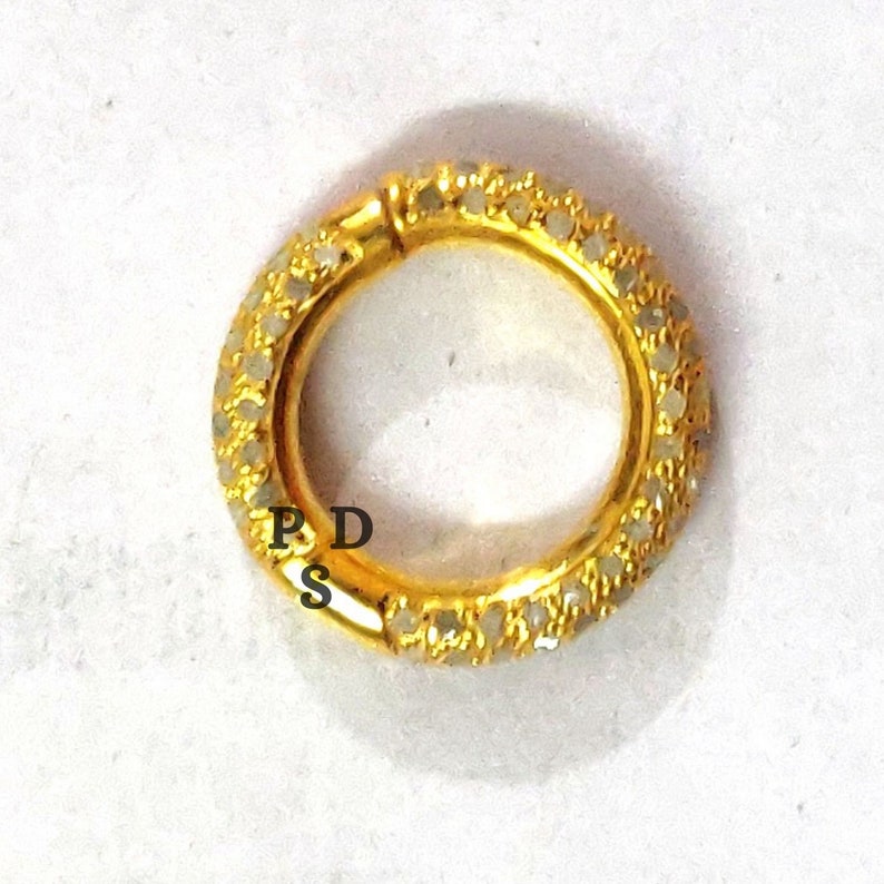 May include: A gold ring with a row of small white stones around the band. The ring is open and has a hinge on one side.