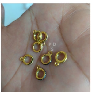 May include: Six gold-toned metal rings with a small loop on one side. Each ring is adorned with small, clear stones. The rings are arranged on a hand.