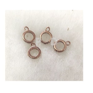 May include: Four gold-toned metal jump rings with a decorative edge. The rings are about 1 inch in diameter and have a small loop at the top for attaching to a chain or other jewelry.