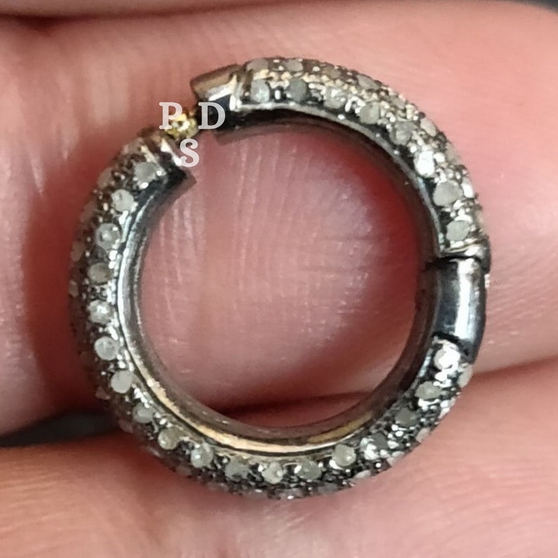 May include: A silver ring with a pave diamond setting. The ring is open and has a hinge closure.
