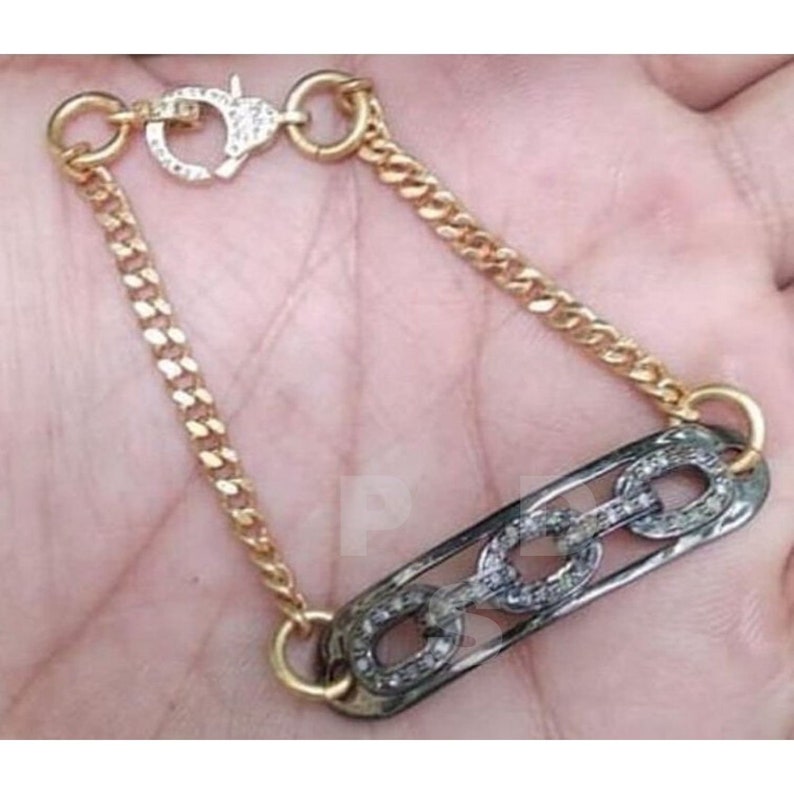May include: A gold chain bracelet with a black metal charm featuring a chain link design with pave set diamonds.