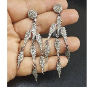 May include: A pair of silver dangle earrings with multiple small diamond-like stones set in each wing-shaped pendant. The earrings are long and have a delicate, feminine look.