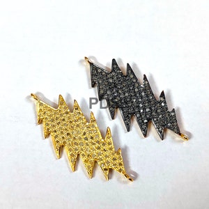May include: Two lightning bolt shaped pendants, one with black diamonds and one with gold diamonds.