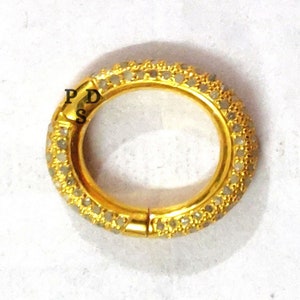May include: A gold ring with a row of small white diamonds around the band. The ring is open and has a hinged clasp.