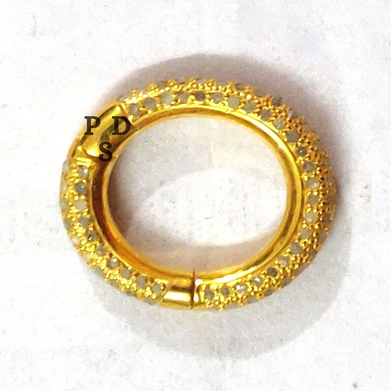 May include: A gold ring with a row of small white diamonds around the band. The ring is open and has a hinged clasp.