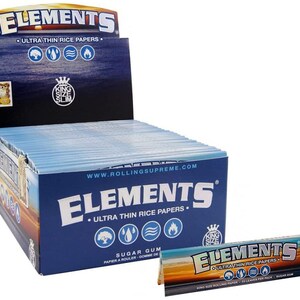 Op de afbeelding: Een doos Elements Ultra Thin Rice Papers, kingsize, met een blauw en wit ontwerp. De doos is open en toont de individuele pakjes met rolpapier. De tekst op de doos luidt "Elements Ultra Thin Rice Papers" en "Sugar Gum".