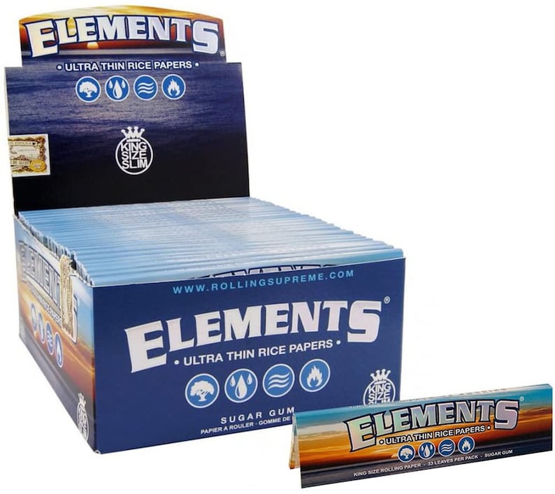 Op de afbeelding: Een doos Elements Ultra Thin Rice Papers, kingsize, met een blauw en wit ontwerp. De doos is open en toont de individuele pakjes met rolpapier. De tekst op de doos luidt "Elements Ultra Thin Rice Papers" en "Sugar Gum".