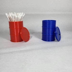 May include: Two small plastic barrels, one red and one blue, with lids. The red barrel is filled with cotton swabs.