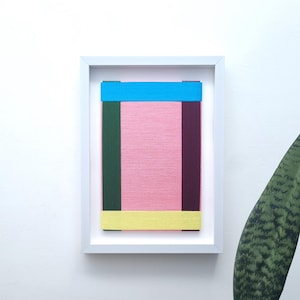May include: A framed abstract art piece with a pink background and colourful stripes of blue, green, yellow, and maroon.