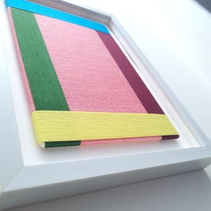 May include: A framed artwork with a geometric design featuring a pink, yellow, green, blue, and burgundy colour scheme.