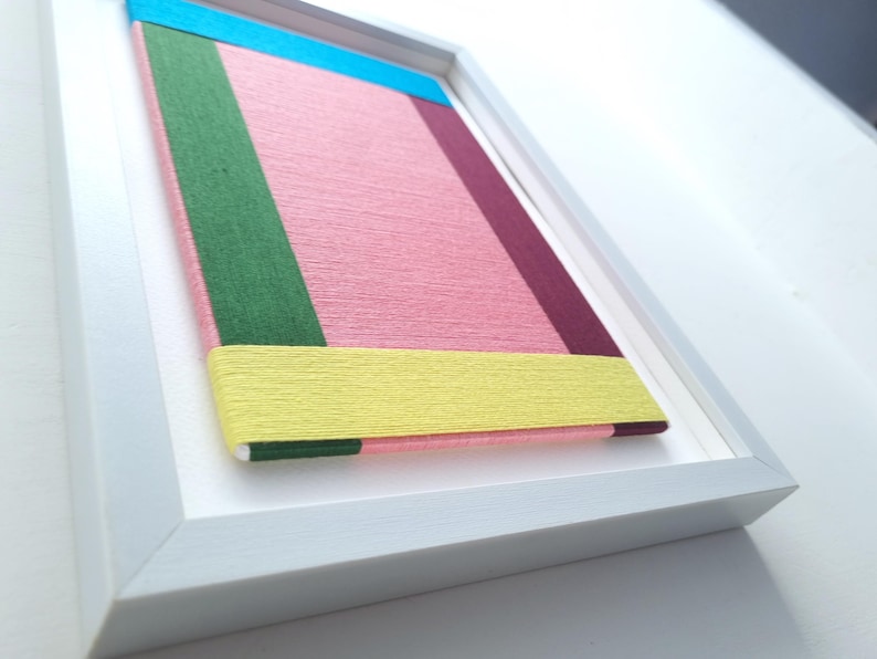 May include: A framed artwork with a geometric design featuring a pink, yellow, green, blue, and burgundy colour scheme.