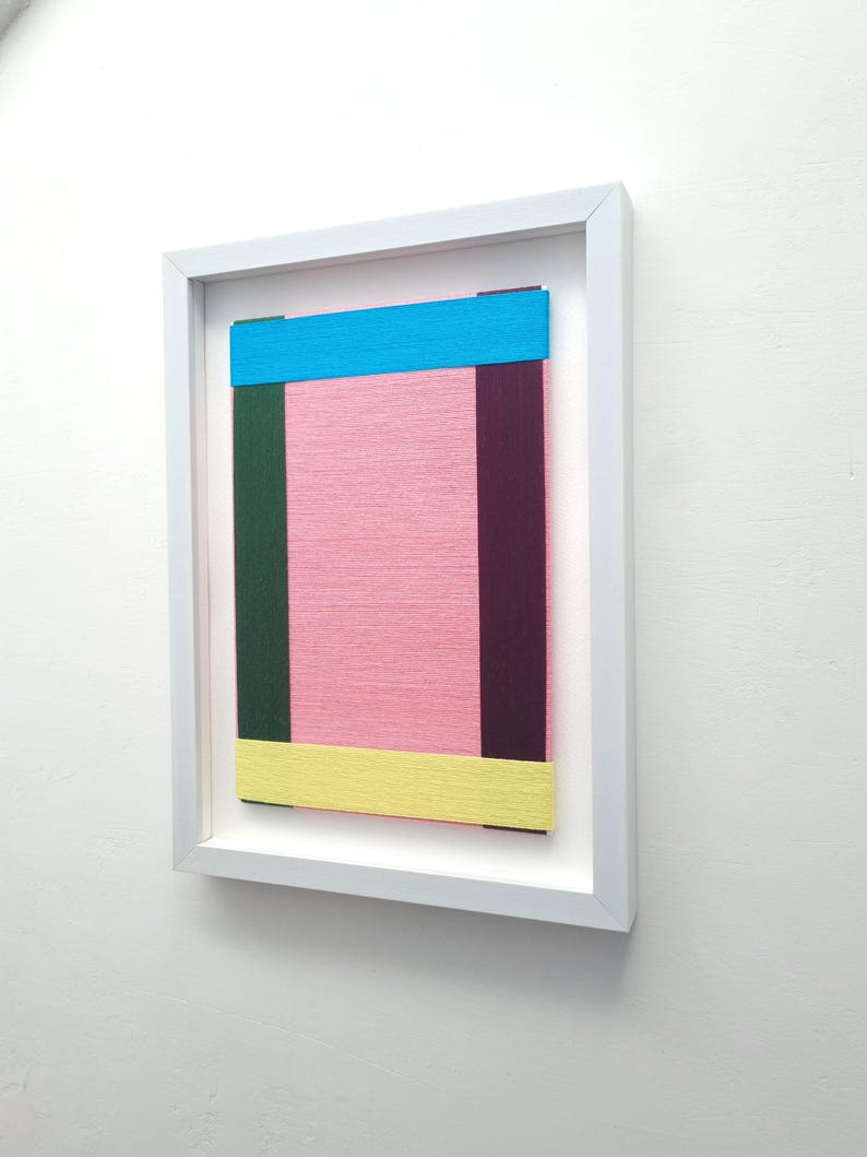 May include: A framed abstract art piece with a pink background and colourful stripes of blue, yellow, green, and purple.