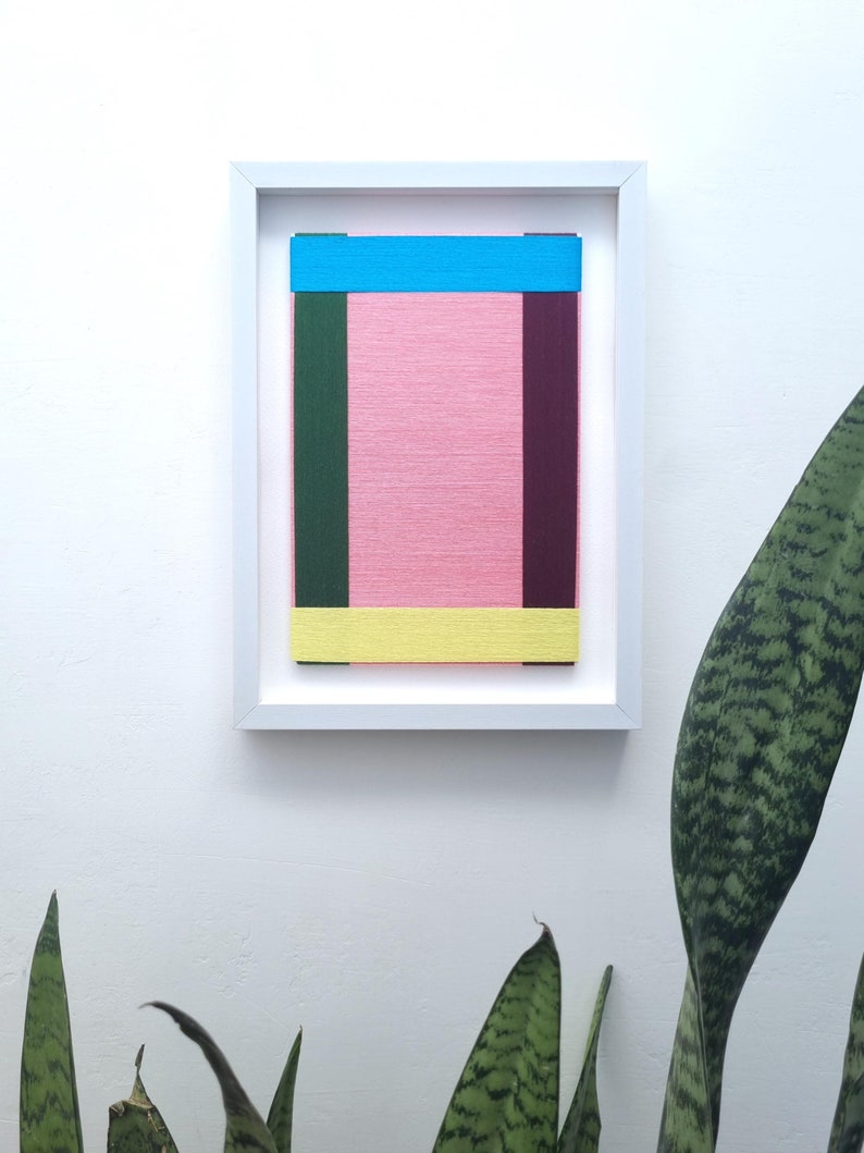 May include: A framed abstract art piece with a pink background and colourful stripes of blue, green, yellow, and maroon.