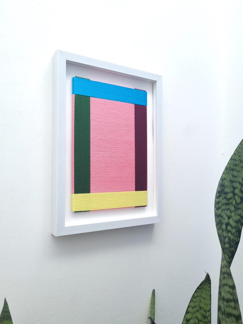May include: A framed abstract art piece with a pink background and colourful stripes in blue, green, yellow, and purple.