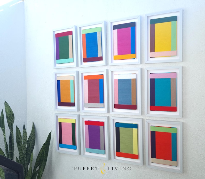 May include: A wall gallery of 12 framed abstract paintings. Each painting features a different combination of colourful geometric shapes and patterns.