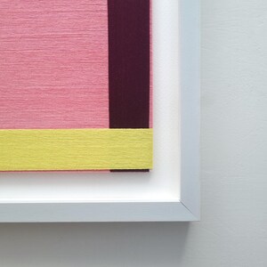 May include: A framed abstract art piece with a pink, yellow, and burgundy colour scheme. The artwork is made of textured fabric.