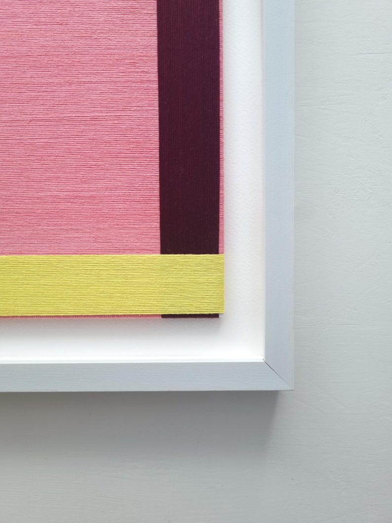 May include: A framed abstract art piece with a pink, yellow, and burgundy colour scheme. The artwork is made of textured fabric.