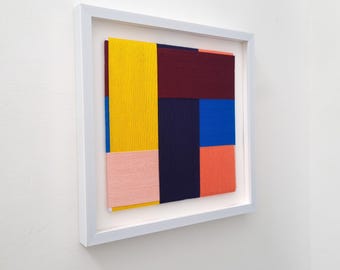 Könnte beinhalten: Ein gerahmtes abstraktes Kunstwerk mit geometrischem Design. Das Kunstwerk zeigt eine Vielzahl von Farben, darunter Gelb, Rosa, Rot, Blau und Lila.