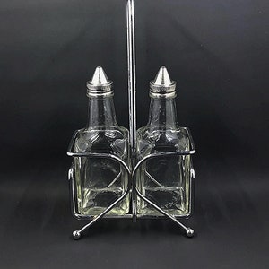 May include: A chrome metal oil and vinegar bottle holder with two clear glass bottles with silver tops.