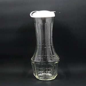 May include: A clear glass bottle with a white plastic lid. The bottle has a textured surface and a narrow neck.