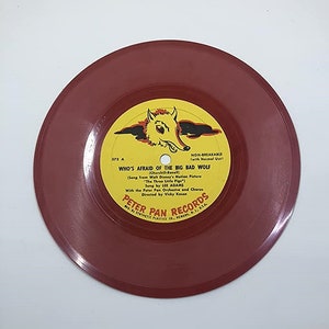 May include: A red vinyl record with a yellow label featuring a cartoon wolf and the text "Who's Afraid of the Big Bad Wolf" from the Walt Disney movie "The Three Little Pigs". The label also includes the text "Peter Pan Records".