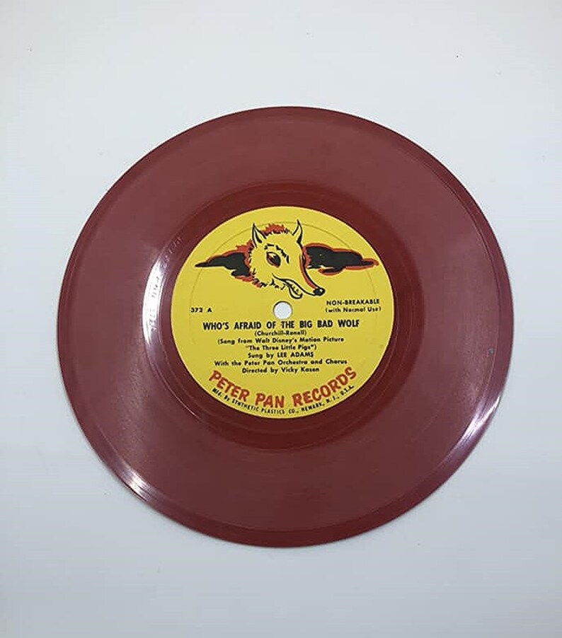 May include: A red vinyl record with a yellow label featuring a cartoon wolf and the text "Who's Afraid of the Big Bad Wolf" from the Walt Disney movie "The Three Little Pigs". The label also includes the text "Peter Pan Records".