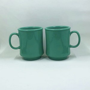 May include: Two teal green ceramic mugs with white interiors and rounded handles.
