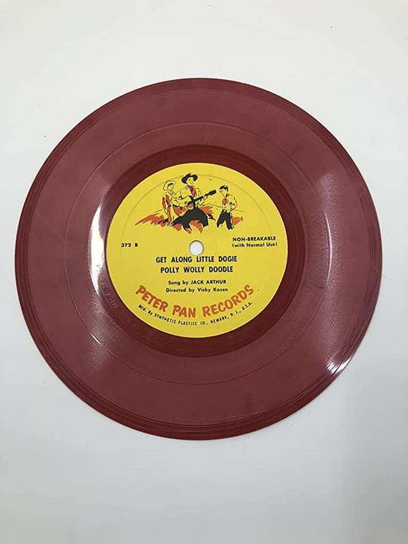 May include: A red vinyl record with a yellow label. The label features a cartoon image of three cowboys on horseback. The text on the label reads "Get Along Little Dogie Polly Wolly Doodle" and "Peter Pan Records".
