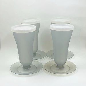 May include: Four gray glass vases with white lids and clear glass bases. The vases are arranged in a row on a white surface.