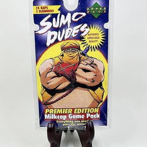 May include: A sealed Sumo Dudes Premier Edition Milkcap Game Pack. The packaging is clear plastic with a blue and yellow label featuring a cartoon sumo wrestler. The pack includes 25 kaps and 2 slammers.