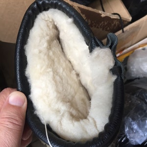Puede incluir: Primer plano del interior de una bota de cuero negro con forro de lana blanca.