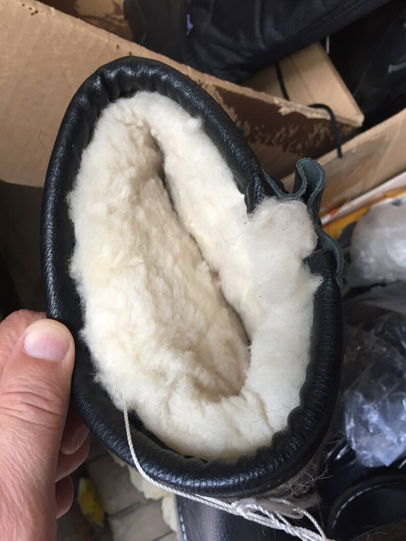 Puede incluir: Primer plano del interior de una bota de cuero negro con forro de lana blanca.