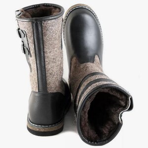 Puede incluir: Un par de botas de cuero negro y fieltro gris con cierre de hebilla. Las botas tienen una suela gruesa y est&aacute;n forradas de piel.