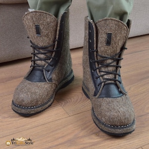 Könnte beinhalten: Ein Paar wadenhohe Stiefel aus brauner Filzwolle mit schwarzen Lederakzenten. Die Stiefel haben schwarze Schnürsenkel, eine abgerundete Zehenpartie und eine dicke schwarze Sohle mit sichtbaren weißen Nähten. Eine kleine schwarze Lasche ist vorhanden.