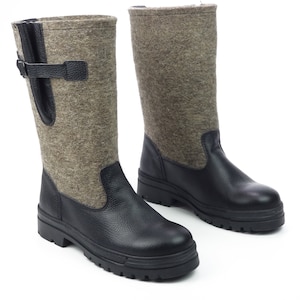 Könnte beinhalten: Ein Paar braune Filzstiefel mit schwarzen Ledereinsätzen und einer dicken schwarzen Gummisohle. Die Stiefel haben einen Schnallenverschluss an der Seite.