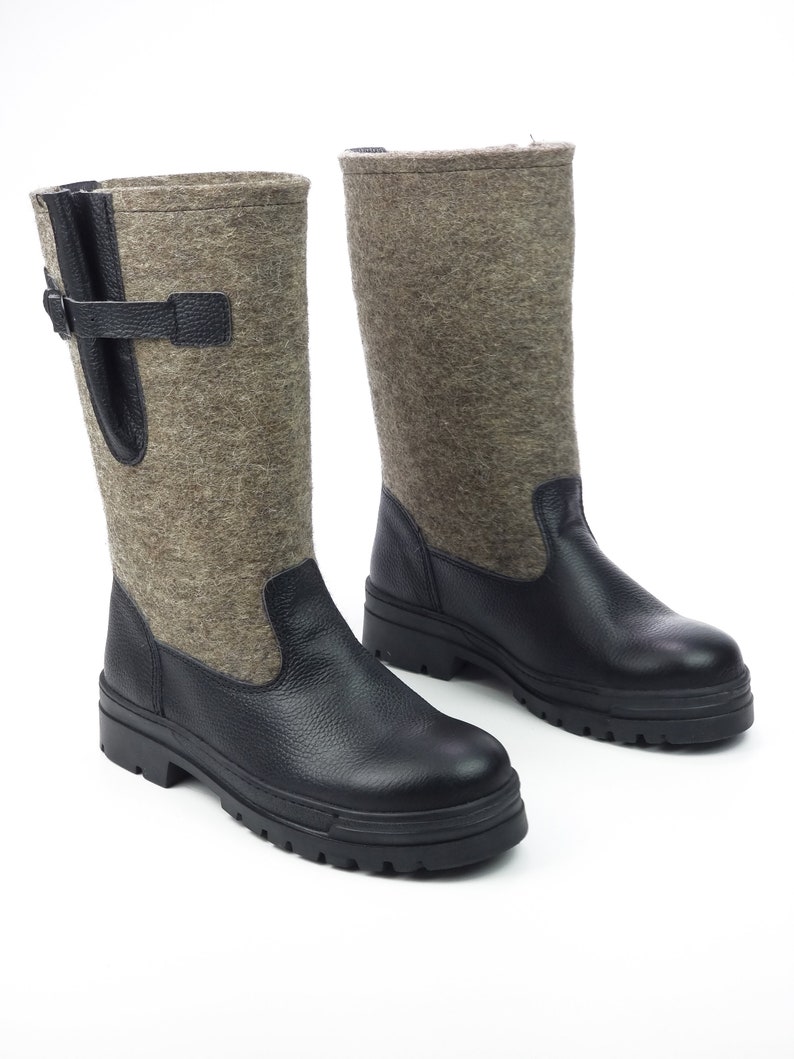 Puede incluir: Un par de botas de media ca&ntilde;a con la parte inferior de cuero negro texturizado y la ca&ntilde;a superior de lana afieltrada gris. Las botas incluyen una tira de cuero negro con una hebilla en el lateral y una suela gruesa de goma negra con tacos.