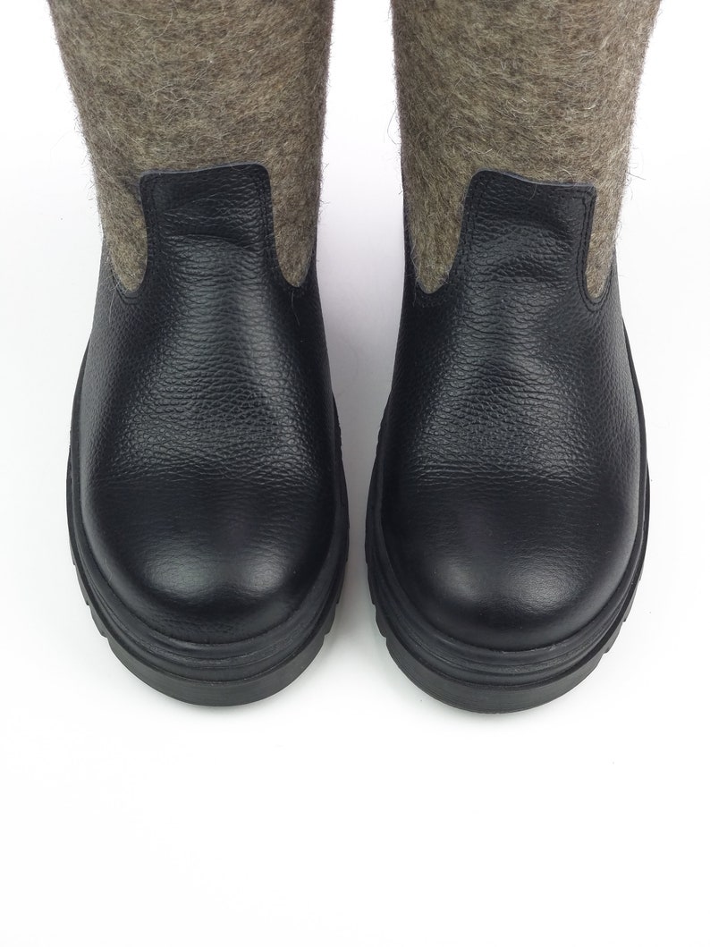 Puede incluir: Un par de botas con secciones inferiores de cuero negro texturizado y ca&ntilde;as superiores de lana afieltrada gris. Las botas tienen punteras redondeadas y suelas negras gruesas, mostrando una combinaci&oacute;n de cuero y lana.