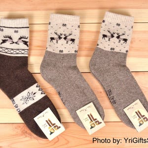 May include: Three pairs of wool socks with a winter theme. One pair is brown with a white snowflake and reindeer design. The other two pairs are gray with a reindeer pattern on the cuff. Each sock has a tag attached.