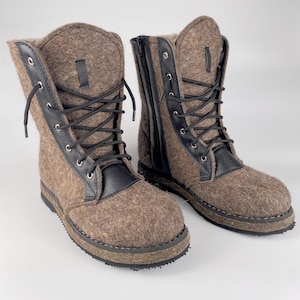 May include: A pair of brown felt boots with black leather accents and laces. The boots have a side zip and a rugged sole.