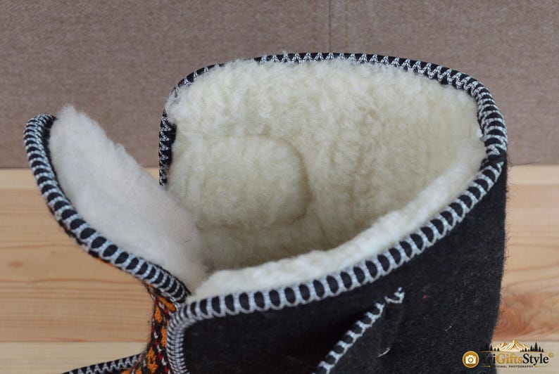 May include: A black felt boot with a thick, cream-colored wool lining. The boot features a high-top design with a wide opening, showcasing the soft interior texture. The edges are finished with a decorative black and white stitched trim.
